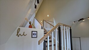 A staircase with wooden steps and white railings, a framed welcome sign, and a small vase with branches.
