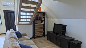 A living room with a sofa, a TV, a staircase, and a bookshelf.