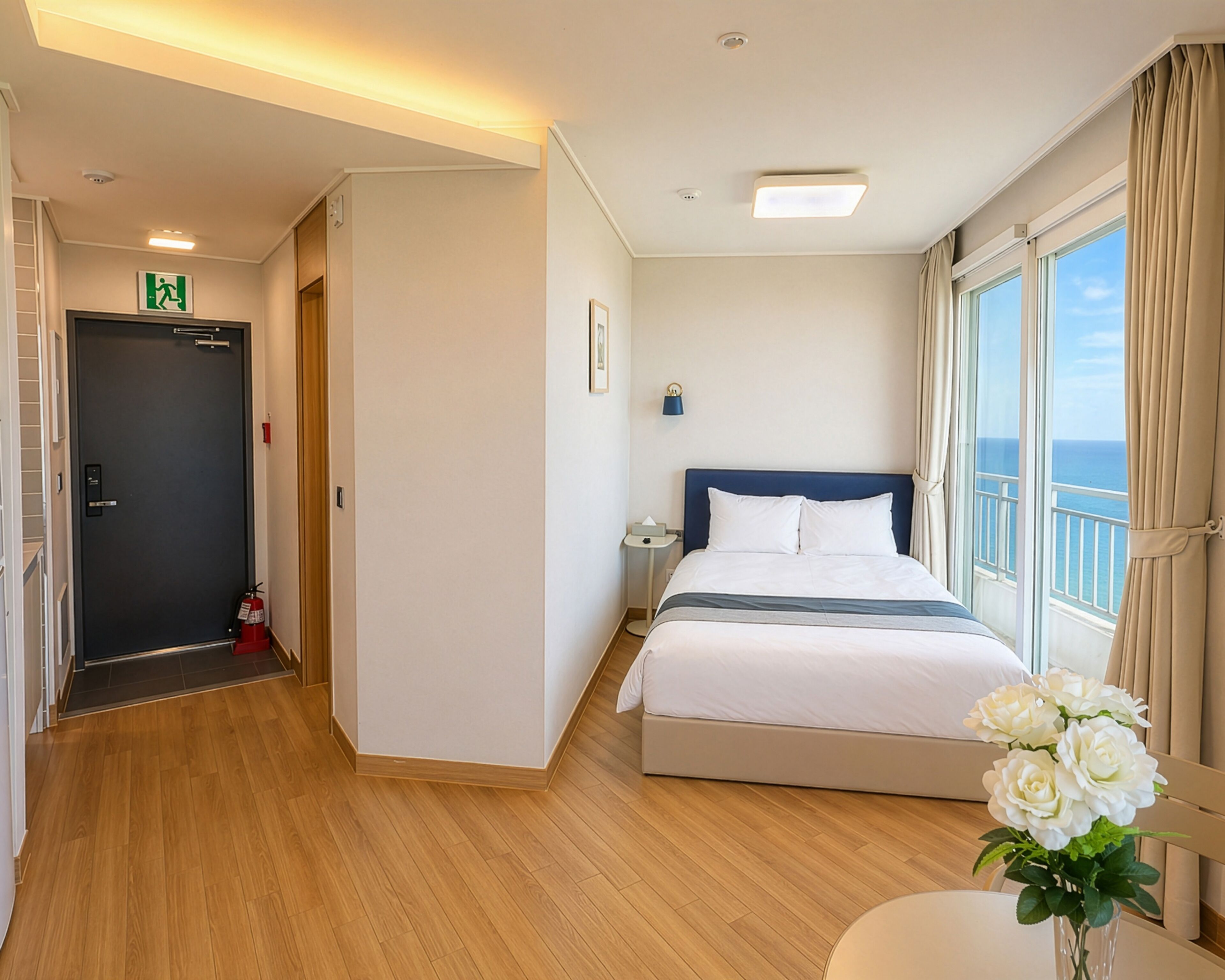 A hotel room with a bed, a nightstand, a window with a view, a door, and a hallway.