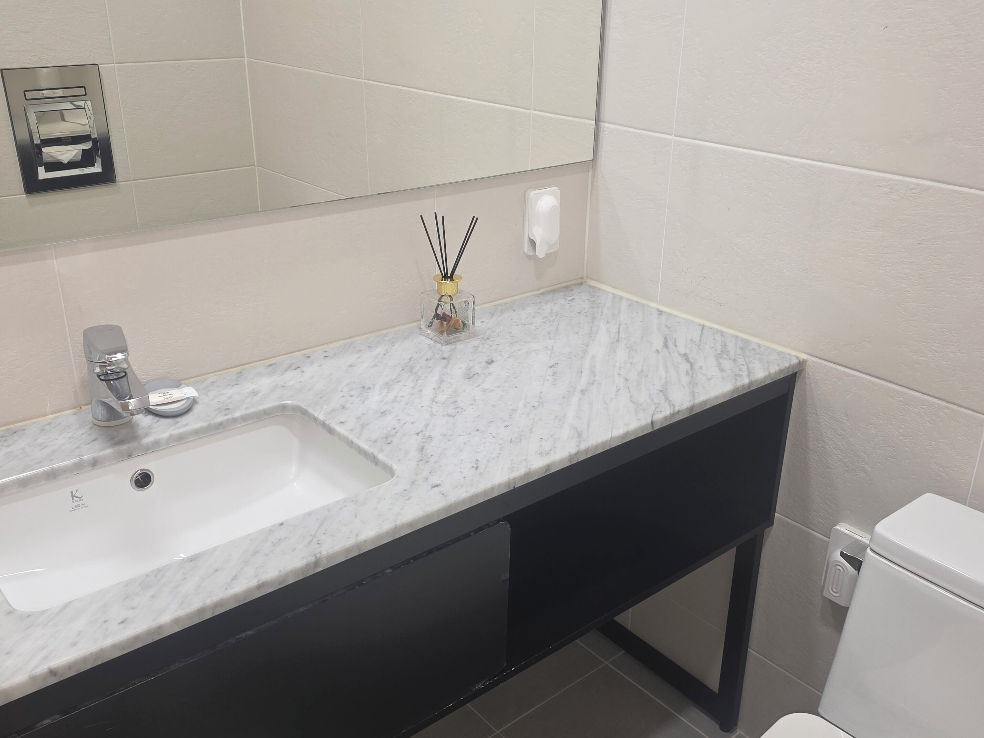 A bathroom with a white sink, a mirror, a black cabinet, and a toilet.