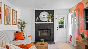 A living room with a fireplace, a sofa, a coffee table, and a door leading outside. - Modern 3BR Home w/ Cowboy Pool + 3-in-1 Game Table (Round Rock)