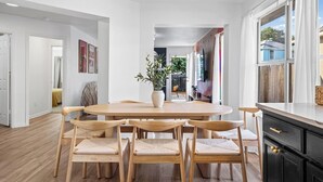 A modern dining area with a wooden table and chairs, a potted plant, and a view of the backyard through large windows. - Modern 3BR Home w/ Cowboy Pool + 3-in-1 Game Table (Round Rock)