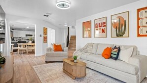A modern living room with a sofa, armchair, coffee table, and artwork on the wall. - Modern 3BR Home w/ Cowboy Pool + 3-in-1 Game Table (Round Rock)