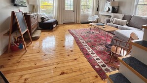 Un vaste salon aménagé dans un style industriel, avec un plancher en bois, une grande fenêtre, un canapé, une table basse et un téléviseur fixé au mur.