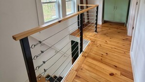 Une pièce avec un plancher en bois, un escalier doté d’une rampe en métal et un meuble contenant des tableaux encadrés.
