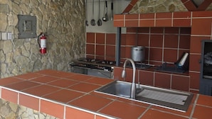 Una cocina con pared de piedra, salpicadero de azulejos, estufa, pileta y utensilios colgantes.