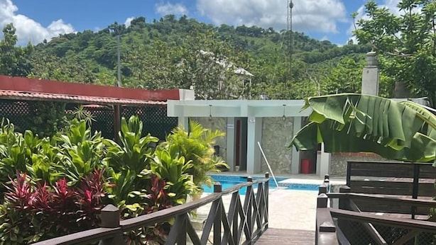Una terraza de madera que da a una zona de piscina con vistas a una montaña y abundante vegetación.
