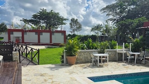 Una piscina con baldosas de piedra y un deck de madera, rodeada de mobiliario exterior y plantas en macetas.