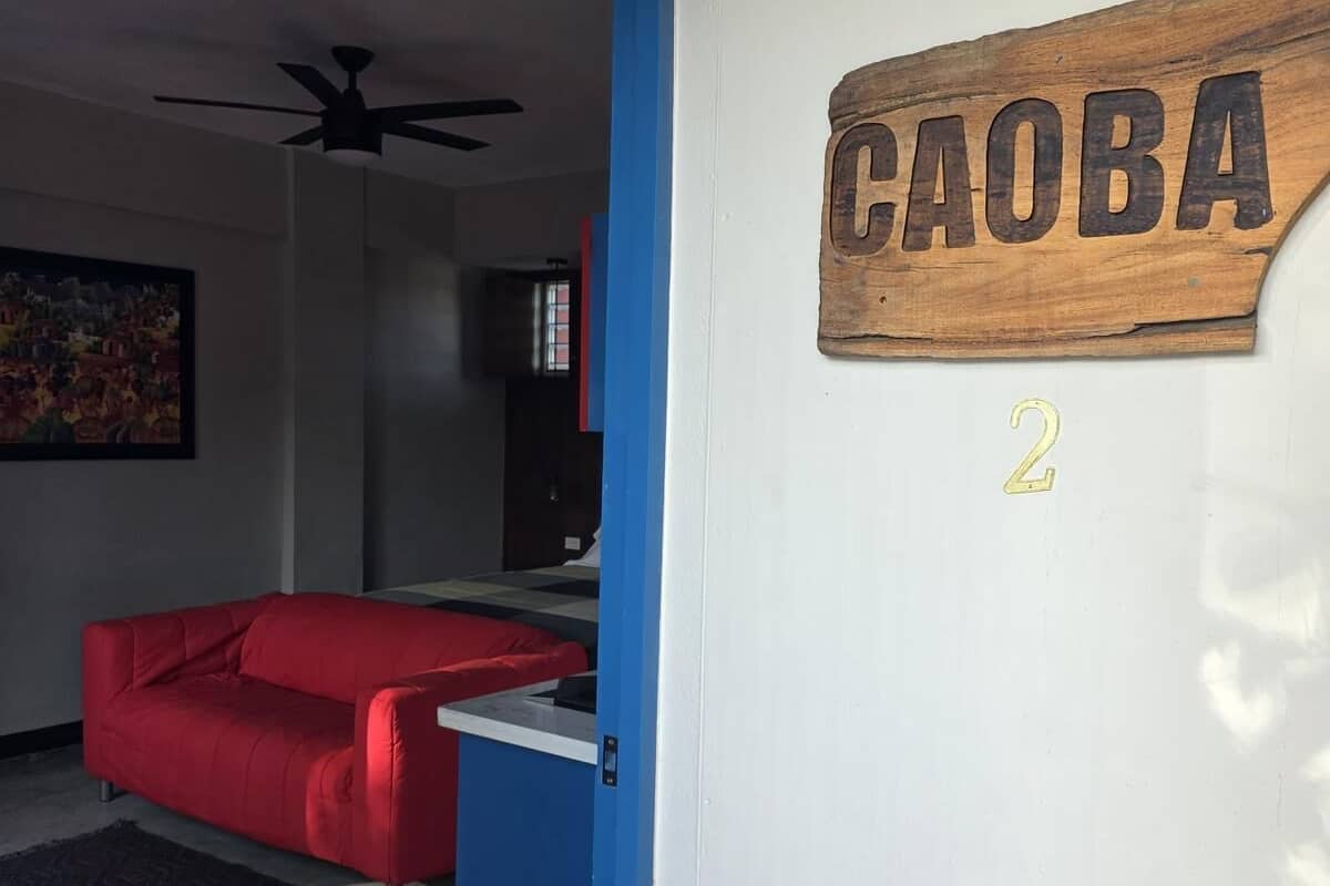 A room with a red sofa, a ceiling fan, a wooden sign with 'CAOBA' and the number '2' on the wall.