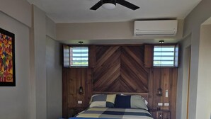 Un dormitorio con cama, ventilador de techo, ventana y aire acondicionado.
