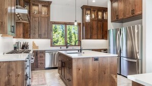 A modern kitchen with wooden cabinets, stainless steel appliances, and a large island. - 85-Acre Luxury Lodge | Theater, Hot Tub, Game Room (Island Park)