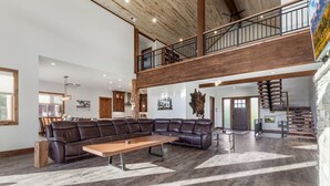 A spacious living area with a large leather sectional sofa, a wooden coffee table, and a staircase leading to an upper level. - 85-Acre Luxury Lodge | Theater, Hot Tub, Game Room (Island Park)