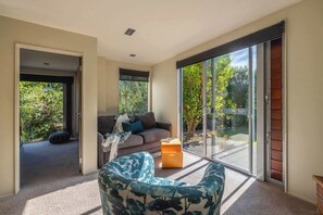 Una sala de estar moderna con un sofá, un sillón estampado y un ventanal corredizo que da a un jardín.