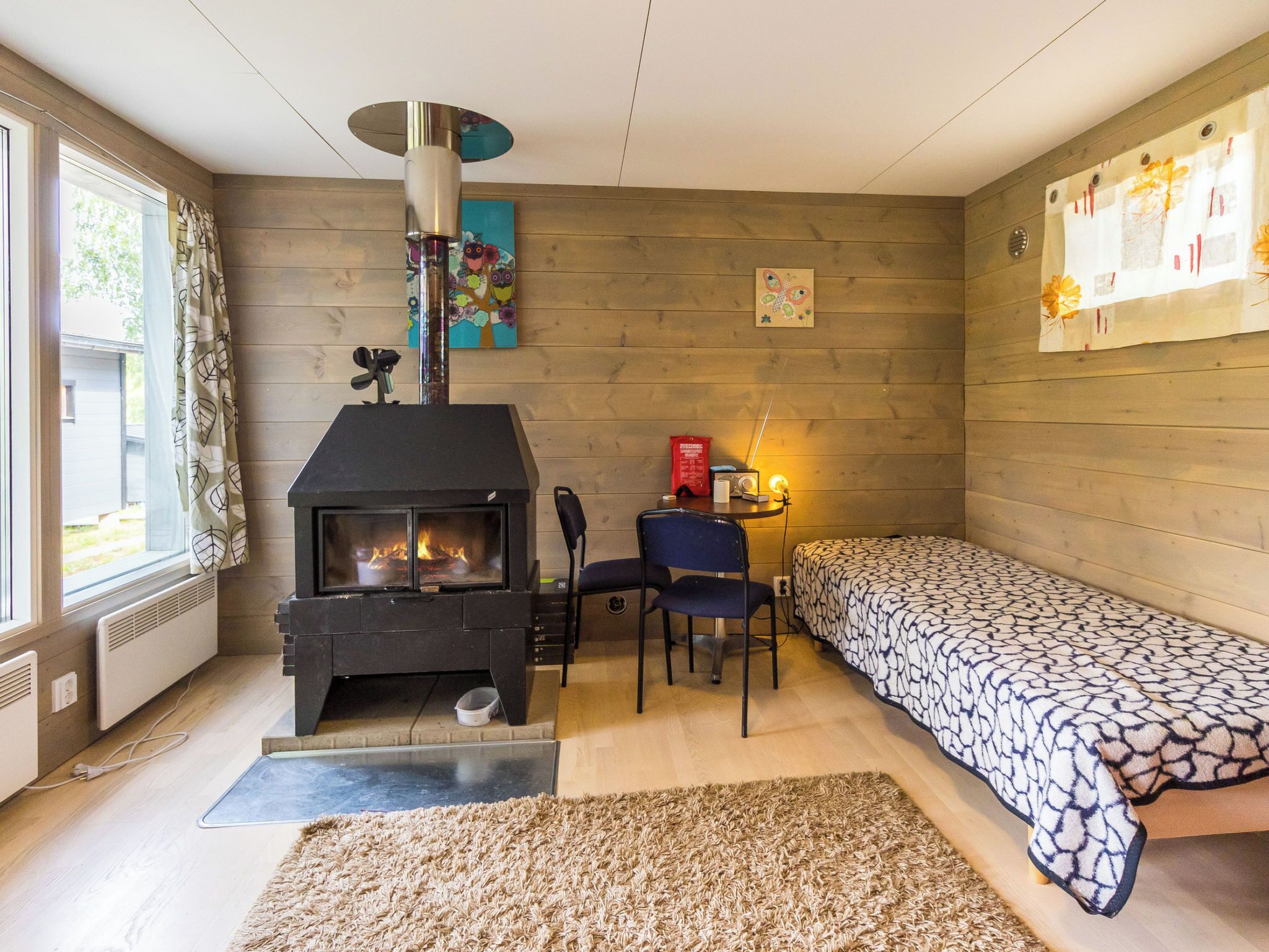 Una habitación acogedora con una chimenea de leña, una cama, un escritorio con una silla y una ventana con cortinas.