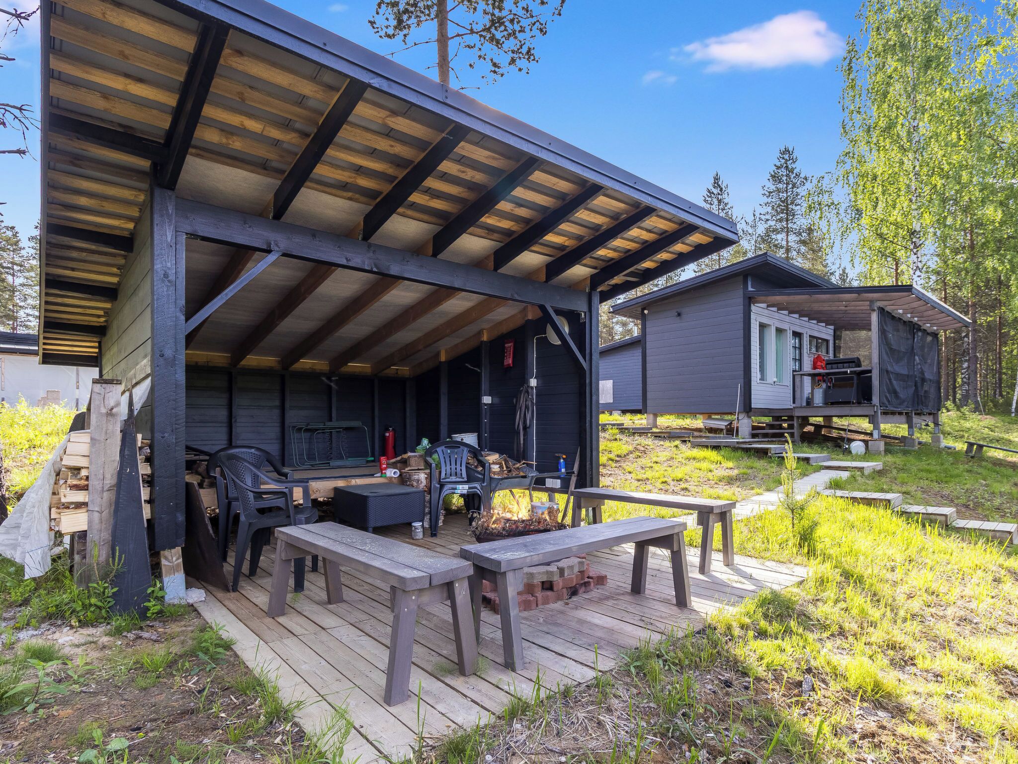 A covered outdoor area with wooden benches and a grill, surrounded by a wooden deck and grassy terrain.