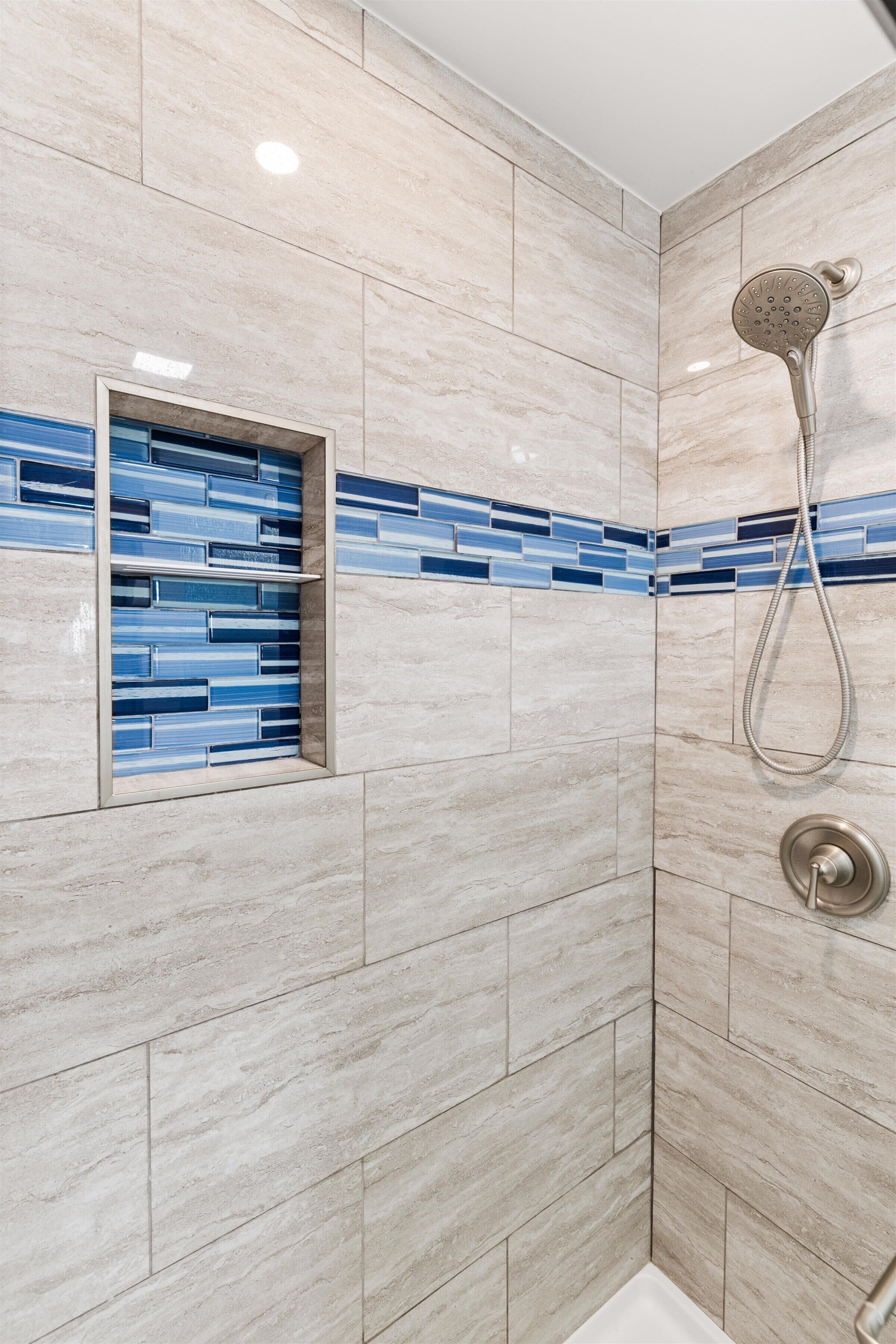 A shower with a handheld showerhead and a wall-mounted control.