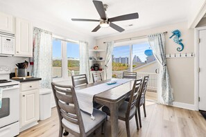 Une cuisine moderne avec des armoires blanches, une table à manger avec des chaises, un ventilateur de plafond et une vue sur la ville grâce à de grandes fenêtres.