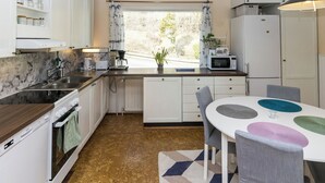 A compact kitchen with a window, white cabinets, a microwave, and a dining area with a patterned rug. - Villa aurinkorinne by Interhome (Fiskars)