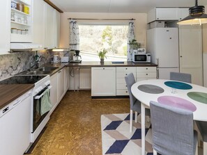 A compact kitchen with a window, white cabinets, a microwave, and a dining area with a patterned rug.