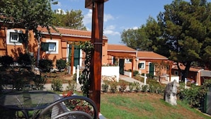 Un edificio residencial con un porche cubierto, un jardín con mesa y sillas de metal, y una estructura de piedra.