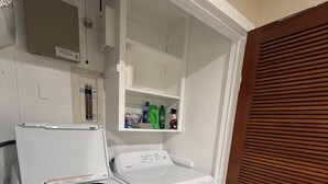 Ett kompakt tvättrum med en tvättmaskin och en torktumlare som man matar från framsidan, en liten hylla med rengöringsmedel och en trädörr.