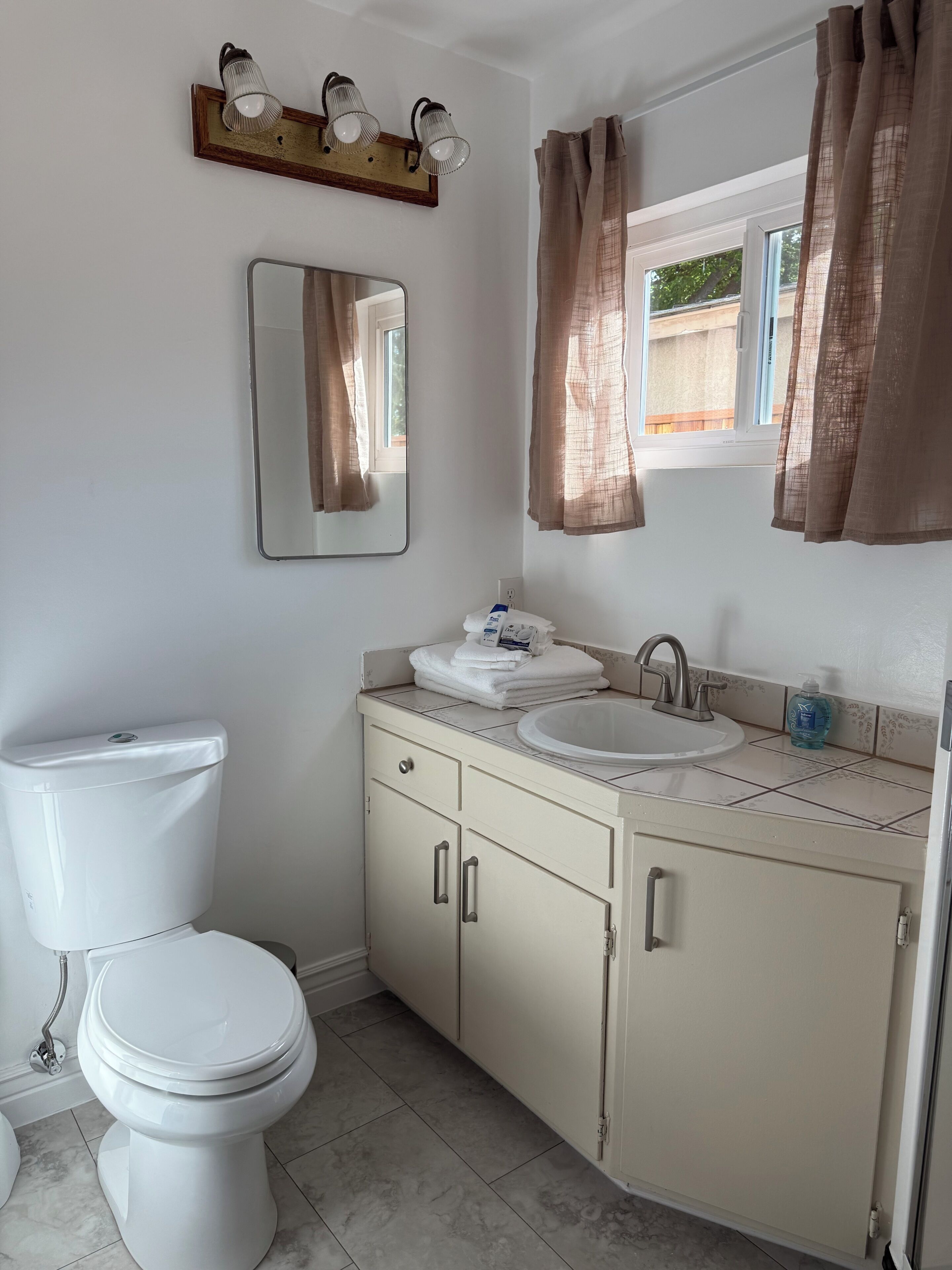 A bathroom with a toilet, sink, mirror, and window with curtains.