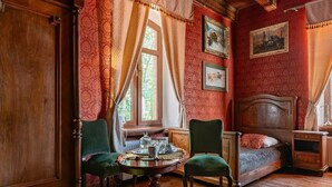 A room with a wooden floor, a round table with chairs, a bed, and a nightstand. - Dwór Mysinek (Bobowo)