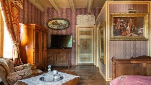 A room with a wooden bed, a wooden cabinet, a television, a table with a lace tablecloth, and a painting on the wall. - Dwór Mysinek (Bobowo)