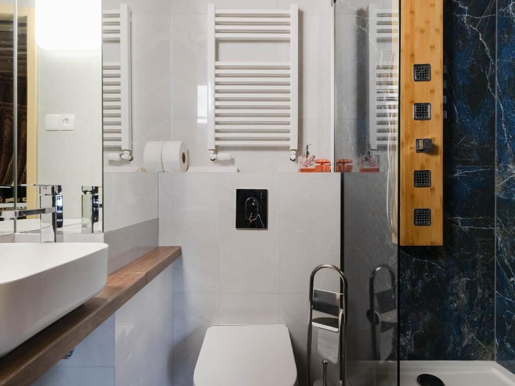 A modern bathroom with a white sink, a glass shower enclosure, and a marble wall.