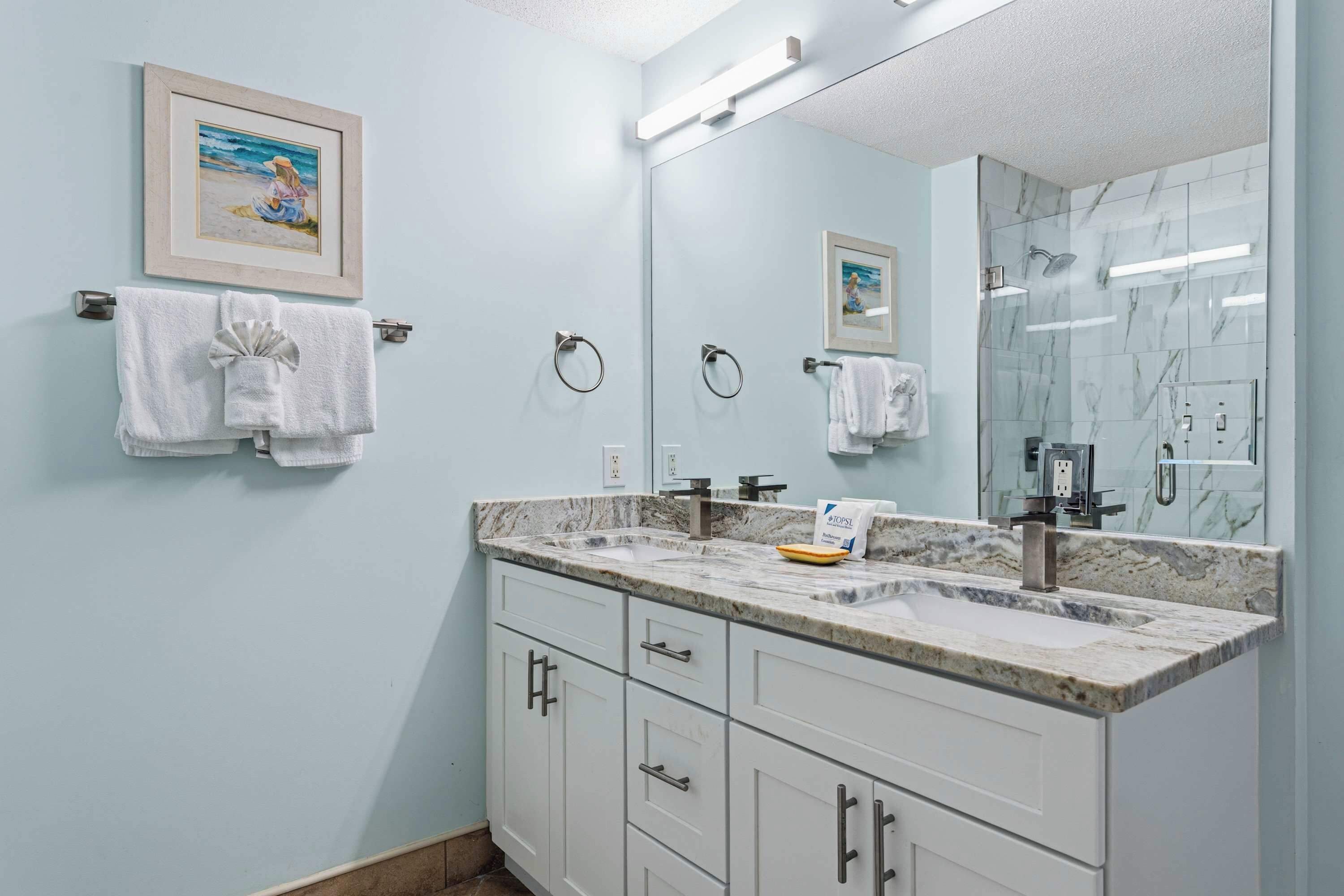 A bathroom with a marble countertop, a sink, a mirror, and two framed pictures on the wall.