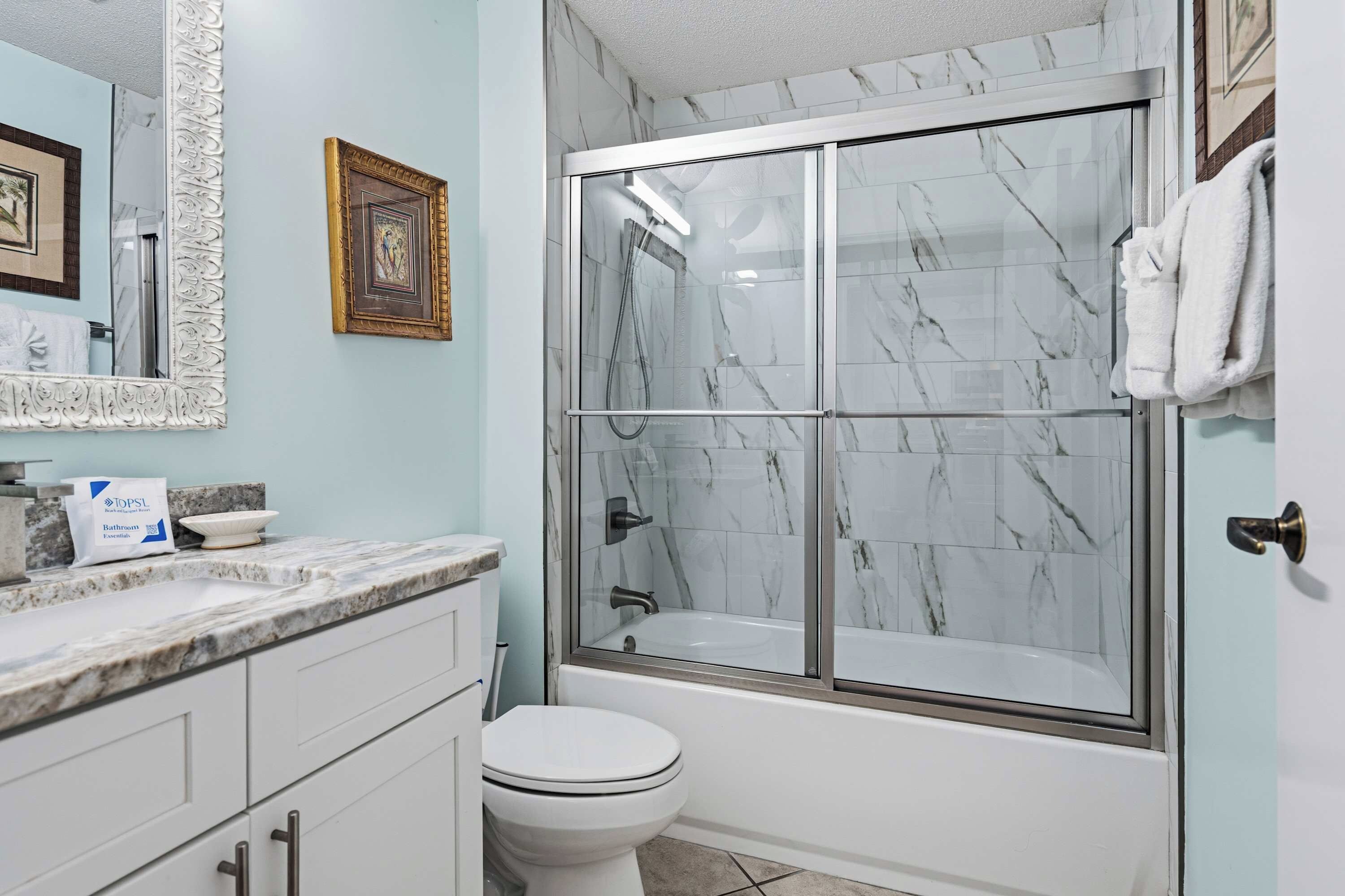 A bathroom with a marble shower enclosure, a toilet, a sink with a marble countertop, and a mirror with an ornate frame.