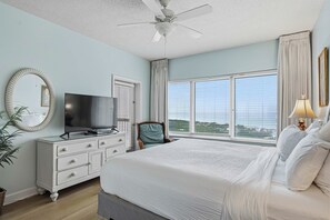A bedroom with a bed, a television, a dresser, a chair, a window with curtains, and a ceiling fan. - Spacious Coastal Escape for Family Getaways (Miramar Beach)