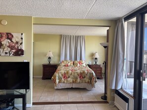 Ein Hotelzimmer mit einem Bett, zwei Nachttischen mit Lampen, einem Flachbildfernseher, einem Deckenventilator und einem großen Fenster mit Vorhängen.