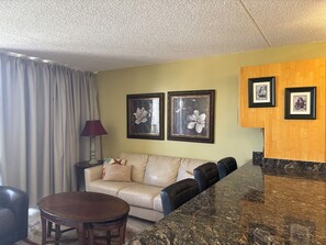 Ein Wohnzimmer mit einer Couch, einem runden Tisch, einer Lampe und gerahmten Kunstwerken an der Wand.
