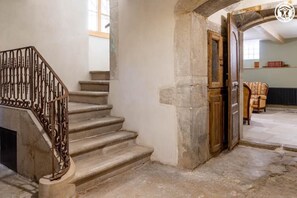 A stone staircase with a wrought iron railing, a wooden door, and a chair in a room with stone walls and a tiled floor. - Stendhal House - LES ECHELLES (LES ECHELLES)