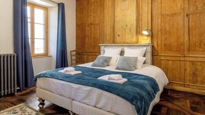 Ein Schlafzimmer mit hölzernem Kopfteil, einem großen Bett mit weißer Bettwäsche und einem Fenster mit blauen Vorhängen.