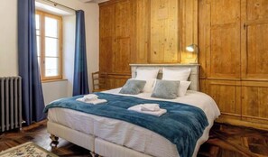 A bedroom with a wooden headboard, a large bed with white bedding, and a window with blue curtains. - Stendhal House - LES ECHELLES (LES ECHELLES)