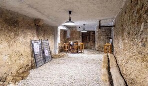 A rustic cellar with stone walls, a wooden barrel table, stools, and a hanging light fixture. - Stendhal House - LES ECHELLES (LES ECHELLES)