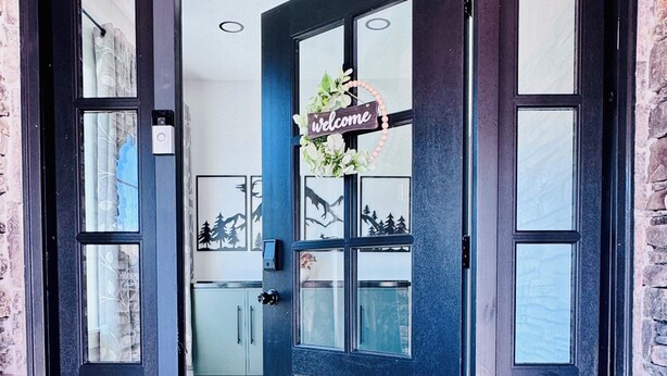 Una puerta negra con un cartel de 'Welcome', un felpudo con la palabra 'hola' y vista a un cuarto con cocina y comedor.