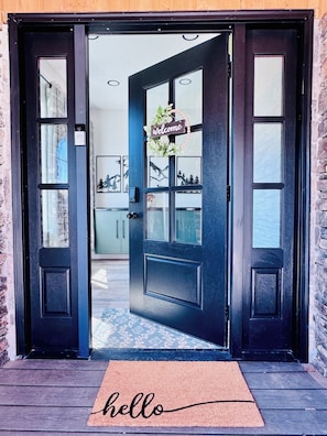 A black door with a 'Welcome' sign, a doormat with 'hello,' and a view into a room with a kitchen and a dining area. - Gorgeous two-bed suite + bonus media room and sleeping loft in updated duplex (Idaho Falls)