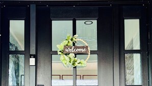 Una puerta oscura con un letrero que dice 'welcome', un felpudo y una cámara de seguridad.