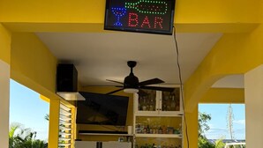 A bar area with a neon sign, a ceiling fan, and a view of the outdoors. - Welcome to Spring Dash,2BR POOL&BEACH ACCESS+VIEW,FREE PARKING,BAR&Grill, &AC (St Ann)