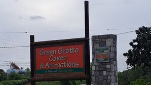 A sign for Green Grotto Caves & Attractions, a National Heritage Site, with a stone wall and tropical plants. - Welcome to Spring Dash,2BR POOL&BEACH ACCESS+VIEW,FREE PARKING,BAR&Grill, &AC (St Ann)