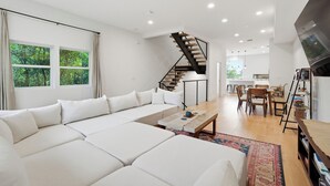 A modern living room with a sectional sofa, a staircase, a dining area, and a kitchen in the background. - Modern 3BR San Marco Villa (Jacksonville)