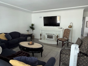 A living room with a sofa, armchair, fireplace, television, and a fan.