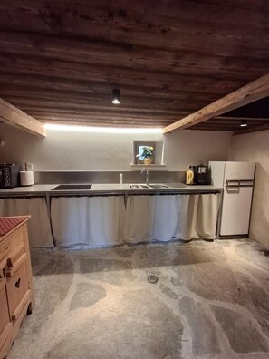 Eine Küche mit Holzboden, eingebautem Spülbecken, kleinem Fenster und Kühlschrank.