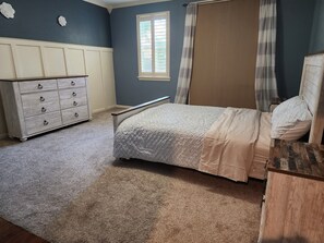 Une chambre à coucher avec un lit, une commode, une fenêtre avec des stores et un rideau.