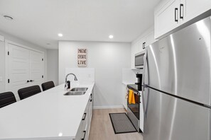 A modern kitchen with a central island, stainless steel appliances, and a motivational wall sign. - The Calgary Stopover (Calgary)
