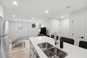 A modern kitchen with a large island, stainless steel appliances, and a dining area with a table and chairs. - The Calgary Stopover (Calgary)