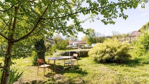 Un jardín con una mesa y sillas, rodeado de follaje y un árbol.